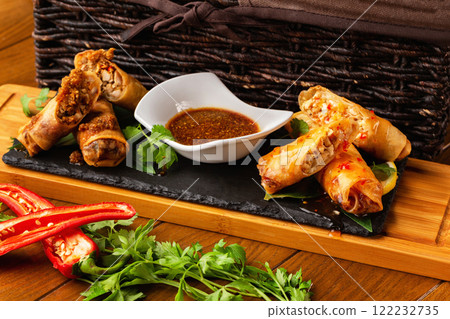 Assortment of asian spring rolls with fresh vegetables and sauce at wooden board at decorated restaurant table background. 122232735
