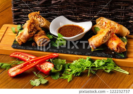 Assortment of asian spring rolls with fresh vegetables and sauce at wooden board at decorated restaurant table background. Assortment of asian spring rolls with fresh vegetables and sauce at wooden board at decorated restaurant table background. 122232737