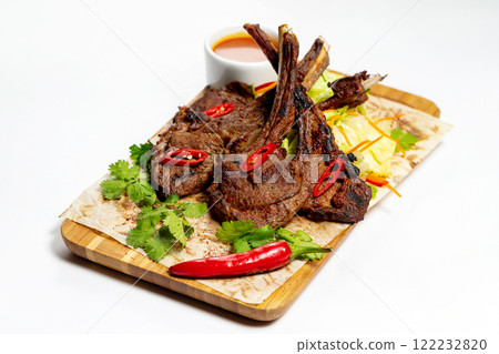 Roasted lamb meat with vegetables and sauce at wooden board with paper isolated at white background. 122232820