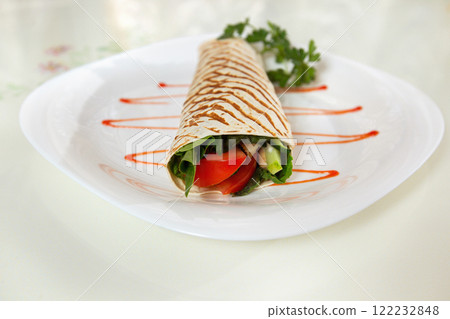 Tasty tortilla roll decorated with sauce on a plate at white background. Concept of healthy meal. 122232848
