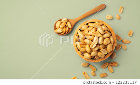 Roasted peanuts in wooden bowl with spoon on green background, top view 122233117