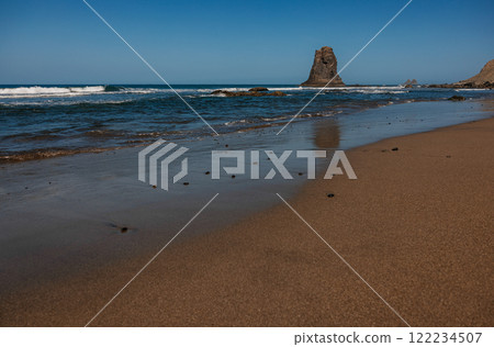 Serene beach with calm waves and a towering rock formation Serene beach with calm waves and a towering rock formation 122234507