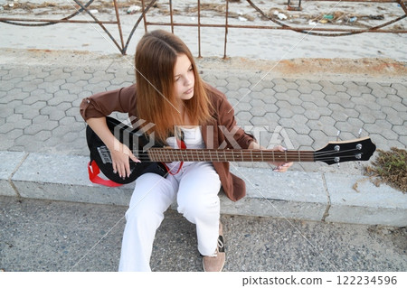 Girl Plays The Bass Instrument Sitting On The Step Near The Street At Evening Girl Plays The Bass Instrument Sitting On The Step Near The Street At Evening 122234596
