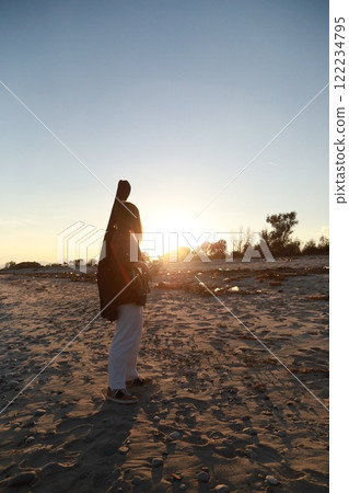 Girl Walks And Plays The Bass Instrument On The Beach Near The Ocean At Sunset 122234795