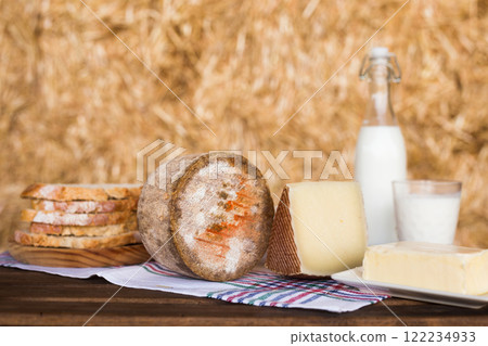 Still life of hard cheese, milk, bread and butter in the hay 122234933