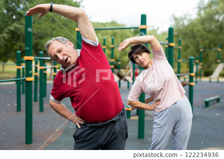 Aged man and woman practicing gymnastics in open-air sports area Aged man and woman practicing gymnastics in open-air sports area 122234936