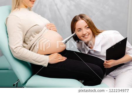 A gynecologist leans a stethoscope to a pregnant woman's belly and listens to the baby's heartbeat A gynecologist leans a stethoscope to a pregnant woman's belly and listens to the baby's heartbeat 122234977