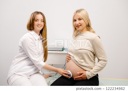 Doctor prepares a pregnant woman for checking fetal heartbeat by fetal monitoring. Doctor prepares a pregnant woman for checking fetal heartbeat by fetal monitoring. 122234982