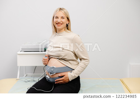 Woman pregnant checking fetal heart beat by fetal monitoring. Expectant mother with midwife adjusting sensors off cardiotocography Woman pregnant checking fetal heart beat by fetal monitoring. Expectant mother with midwife adjusting sensors off cardiotocography 122234985