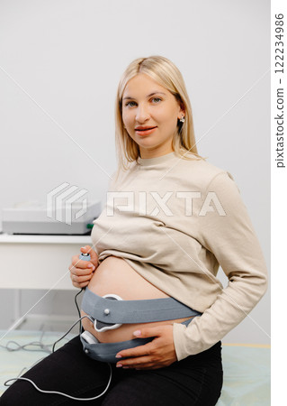 Woman pregnant checking fetal heart beat by fetal monitoring. Expectant mother with midwife adjusting sensors off cardiotocography Woman pregnant checking fetal heart beat by fetal monitoring. Expectant mother with midwife adjusting sensors off cardiotocography 122234986