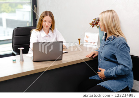 Young pregnant woman visiting her gynecologist in modern clinic. Woman sitting on chair and talking to her doctor 122234993