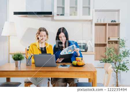 Two Woman sitting in the kitchen at home office reviewing and discussing a business project. Two Woman sitting in the kitchen at home office reviewing and discussing a business project. 122235494