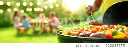 A vibrant summer barbecue scene with burgers and vegetables grilling, while family and friends enjoy a meal 122235655