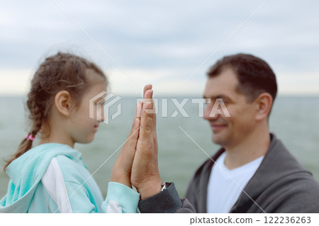 Joined palms of happy father and daughter in blur against sea Joined palms of happy father and daughter in blur against sea 122236263