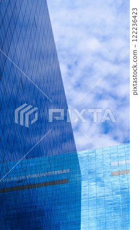 Urban Reflection. Strikingly sharp angles of a glass skyscraper reflecting the dynamic patterns of clouds, illustrating the harmony between modern architecture and nature 122236423