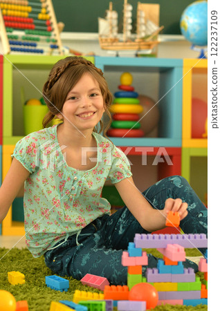 Portrait of cute girl playing with colorful plastic blocks in room Portrait of cute girl playing with colorful plastic blocks in room 122237109