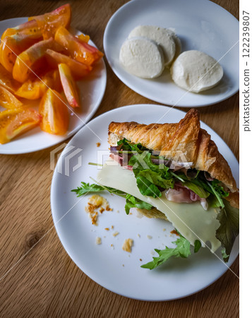 Delicious croissant sandwich with salad, cheese and ham served with fresh tomatoes and mozzarella cheese slices Delicious croissant sandwich with salad, cheese and ham served with fresh tomatoes and mozzarella cheese slices 122239807