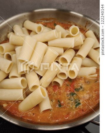 Rigatoni pasta added to tomato sauce in stainless steel pan 122240144