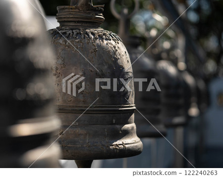 Traditional antique bells hang in an outdoor temple in Thailand. Close-up of beautiful bells lined up in a Buddhist temple or place in Thailand. Calm and believe. Traditional antique bells hang in an outdoor temple in Thailand. Close-up of beautiful bells lined up in a Buddhist temple or place in Thailand. Calm and believe. 122240263