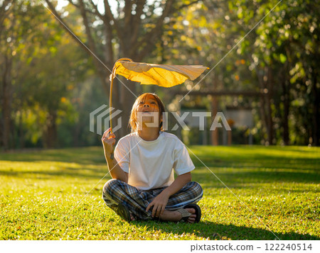 Happy little girl outdoors in nature and having fun picking leaves with beautiful warm sunset in the park. 122240514