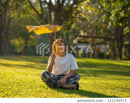 Happy little girl outdoors in nature and having fun picking leaves with beautiful warm sunset in the park. Happy little girl outdoors in nature and having fun picking leaves with beautiful warm sunset in the park. 122240515