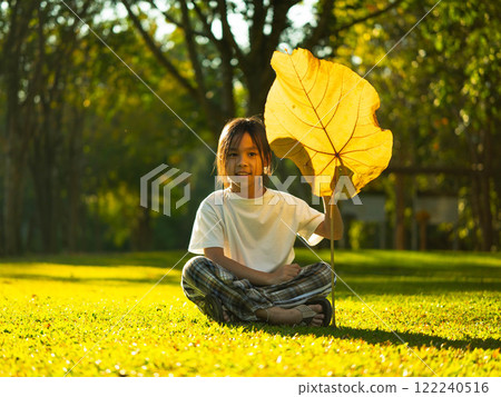 Happy little girl outdoors in nature and having fun picking leaves with beautiful warm sunset in the park. Happy little girl outdoors in nature and having fun picking leaves with beautiful warm sunset in the park. 122240516