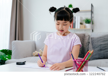 A cute little girl is drawing and coloring with colored pencil on a piece of paper A cute little girl is drawing and coloring with colored pencil on a piece of paper 122240782