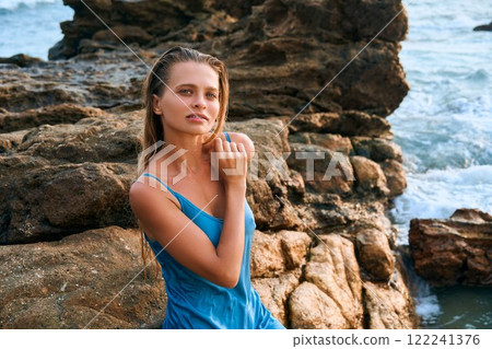 Stunning model in wet dress, rocky shore, exotic island backdrop. Ocean waves crash, luxury fashion scene. Woman elegance, grace. Beauty, cosmetics, fragrance themes. Tropical allure. Stunning model in wet dress, rocky shore, exotic island backdrop. Ocean waves crash, luxury fashion scene. Woman elegance, grace. Beauty, cosmetics, fragrance themes. Tropical allure. 122241376