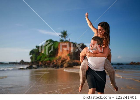 Joyful woman enjoys piggyback ride on man's back, couple on beach at sunset, playful date by sea, love, fun romantic moment, vacation together, smartphone dating app success, seaside bonding Joyful woman enjoys piggyback ride on man's back, couple on beach at sunset, playful date by sea, love, fun romantic moment, vacation together, smartphone dating app success, seaside bonding 122241401