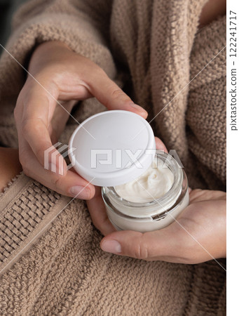 Closeup of woman in brown bathrobe opening white cream jar with hands, cosmetic mockup Closeup of woman in brown bathrobe opening white cream jar with hands, cosmetic mockup 122241717