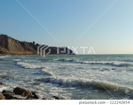 beautiful sea view of rocky shore and blue foamy sea with calm surf on sunny day, landscape of bay with foam on calm waves and high cliff on beach 122242654