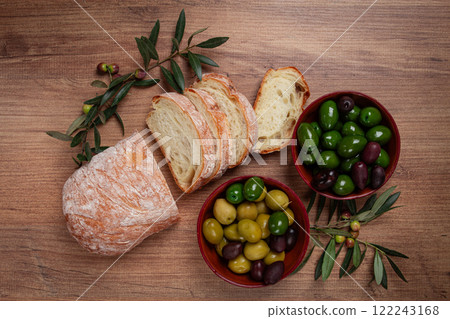 a mixture of olives, varieties of Halkidiki, Verdi giganti and Kalamata, in a bowl, with sliced ciabata bread, top view, no people, 122243168