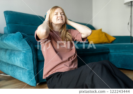 Depressed young woman sitting near couch in the living room at home, Frustrated confused female feels unhappy problem in personal life. Exhausted girl portrait suffering migraine. Hand on head. Depressed young woman sitting near couch in the living room at home, Frustrated confused female feels unhappy problem in personal life. Exhausted girl portrait suffering migraine. Hand on head. 122243444