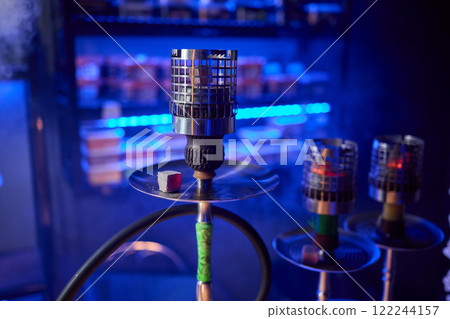 Close up of a hookah made of metal and glass on a wooden table Close up of a hookah made of metal and glass on a wooden table 122244157