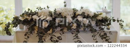 Banner table with a white tablecloth and a floral arrangement of white flowers 122244334