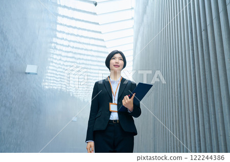 一位身穿西裝的女商人在辦公室走動時操作智慧型手機 122244386