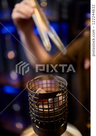 Close up of a hookah made of metal and glass on a wooden table Close up of a hookah made of metal and glass on a wooden table 122244632