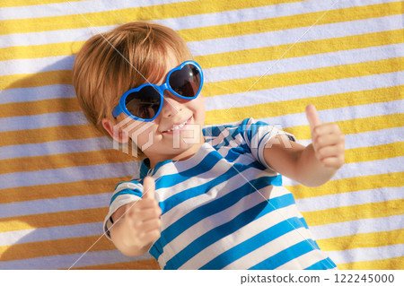 Top view portrait of happy child lying on beach towel on summer vacation Top view portrait of happy child lying on beach towel on summer vacation 122245000