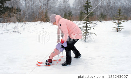 Young mother helps her daughter ski for the first time in snowy weather, sharing a joyful experience on the slopes in the winter outdoors Young mother helps her daughter ski for the first time in snowy weather, sharing a joyful experience on the slopes in the winter outdoors 122245007