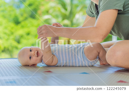 A mother practices baby gymnastics with her 3-month-old on a soft children's play mat. A joyful and nurturing moment focused on bonding, development, and care. Early childhood, fitness, and parenting 122245079