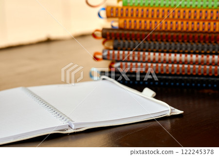 Open White Spiral Notebook with Colorful Notebooks in Background. 122245378