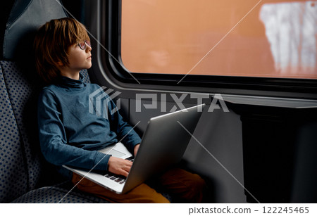 Boy Sitting on Train Seat with Laptop and Looking Outside. 122245465