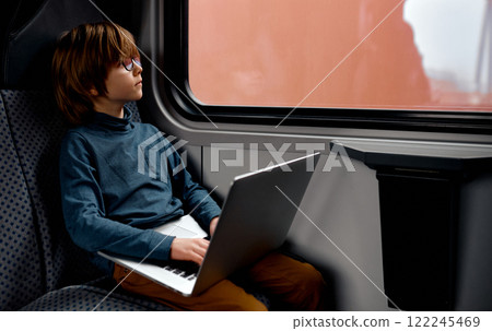Young Boy with Laptop Gazing Through Train Window. 122245469