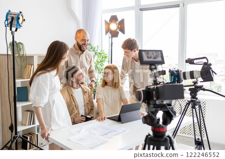 Coworkers cooperation. Happy team. Smiling colleagues work paper documents front of video cameras. Collaboration photography in lighted studio. 122246552