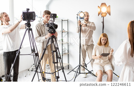 Backstage studio. Team work. Art crew preparing for interview in brightly lit room. Photo video shooting with professional equipment. 122246611