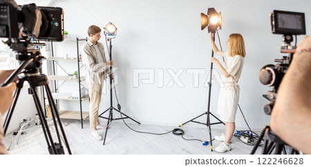 Studio equipment. Team work. Man woman setting up spotlights. Background advertising preparation for professional video shooting free space. Studio equipment. Team work. Man woman setting up spotlights. Background advertising preparation for professional video shooting free space. 122246628