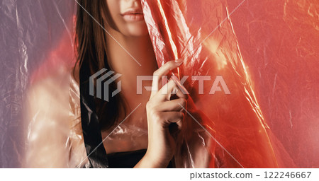 Woman protection. Female insecurity. Cropped art portrait of scared disturbed girl hiding behind wrinkled texture polyethylene film drop on defocused coral pink. 122246667