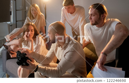 Backstage team. Shoot discuss. Art director sits with assistants on couch explain project ideas. Concept modern friendly photo studio work. 122246698