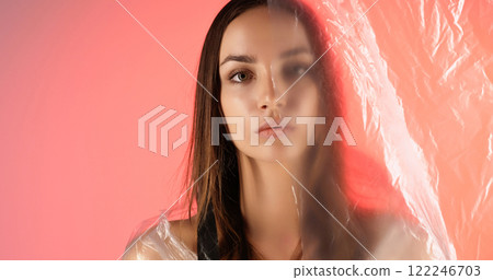 Confident female. Woman rights. Serious girl wearing transparent polyethylene cloak isolated on coral pink color gradient glow light copy space background. 122246703