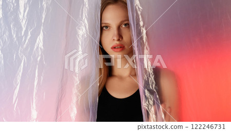 Female character. Gorgeous woman. Disturbed insecure girl hiding behind wrinkled polyethylene film on pink blue color gradient glow out of focus background. Female character. Gorgeous woman. Disturbed insecure girl hiding behind wrinkled polyethylene film on pink blue color gradient glow out of focus background. 122246731
